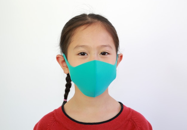 La bambina asiatica ravvicinata indossa una maschera facciale per proteggere dalla diffusione di covid-19 o coronavirus isolato su sfondo bianco