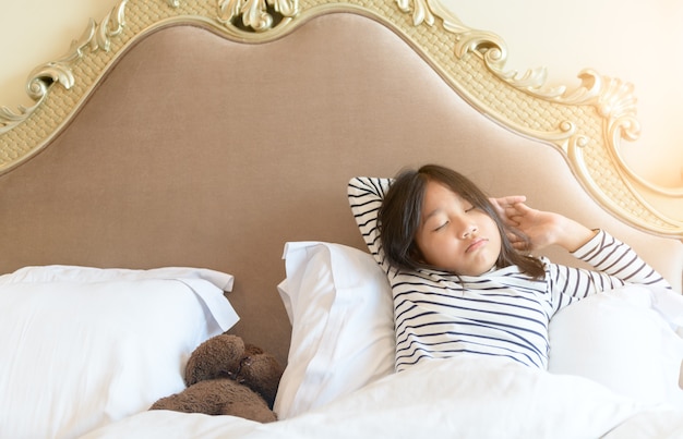 La bambina asiatica si sveglia e si estende sul letto la mattina, concetto sano