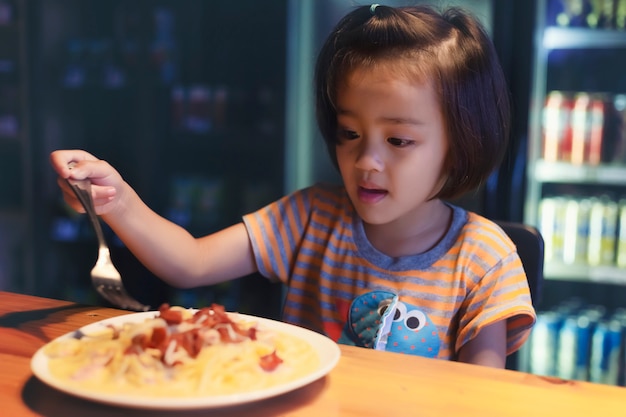 La bambina asiatica sta mangiando gli spaghetti bolognese nel ristorante felicemente.