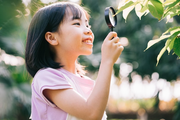 La bambina asiatica sta usando la lente d'ingrandimento per giocare nel parco