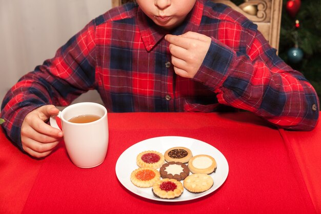 La bambina beve tè e biscotti sullo sfondo dell'albero di Natale