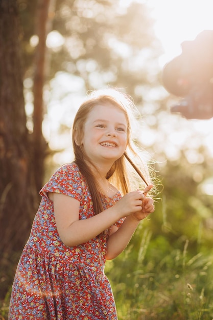 La bambina bionda in abito di mussola beige tiene i chicchi di grano nel palmo della sua mano nel campo di grano al tramonto