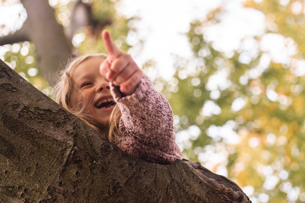 La bambina bionda sorridente punta il dito mentre si trova su un albero