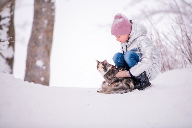 La bambina cammina con il gatto al guinzaglio in un parco invernale innevato