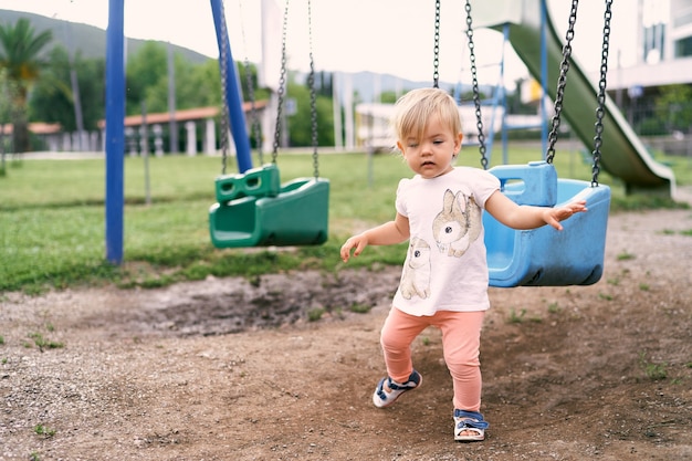 La bambina cammina nel parco giochi sullo sfondo di un'altalena