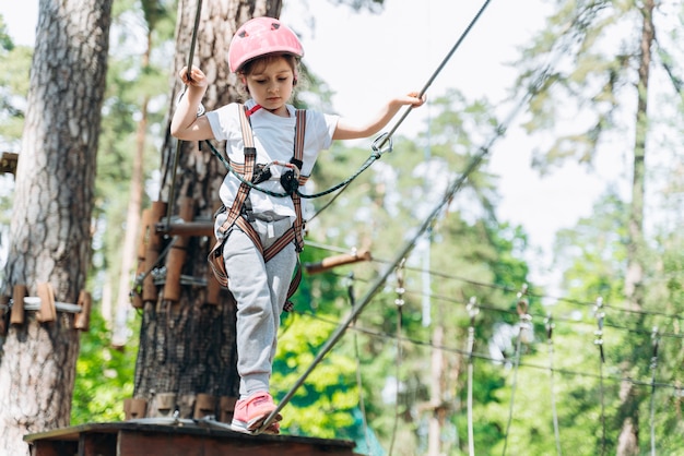 La bambina cammina su una corda, le mani che tengono una corda. Un bambino in un parco avventura supera gli ostacoli