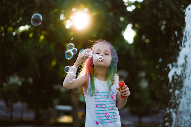 la bambina carina caucasica sta soffiando bolle di sapone nel parco