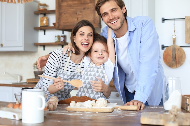 La bambina carina e i suoi genitori si divertono mentre cucinano insieme in cucina a casa.