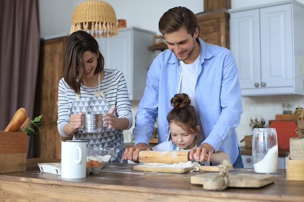 La bambina carina e i suoi genitori si divertono mentre cucinano insieme in cucina a casa.