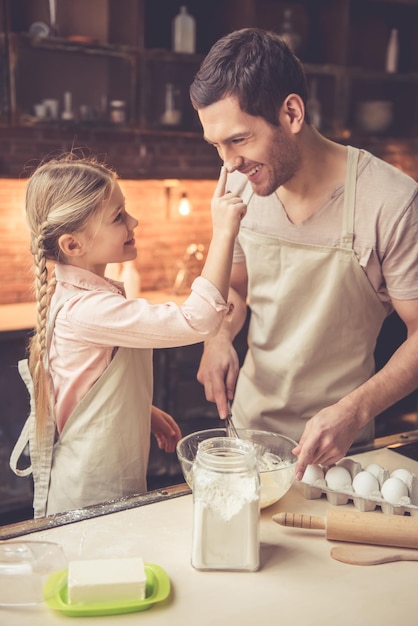 La bambina carina e il suo bel papà in grembiule si divertono mentre cuociono in cucina a casa