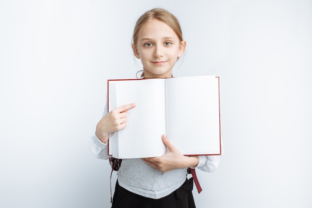 La bambina carina è una studentessa, indicando il libro, muro bianco