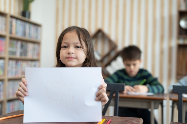 La bambina carina usa la matita colorata disegnando la sua famiglia su carta e mostra all'insegnante in classe a scuola