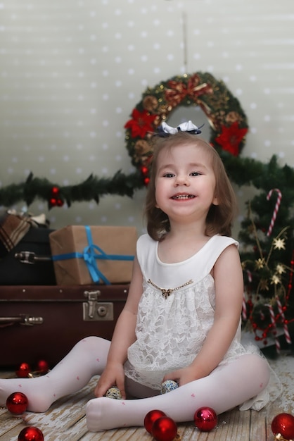 La bambina carina veste l'albero di Natale sul pavimento della stanza