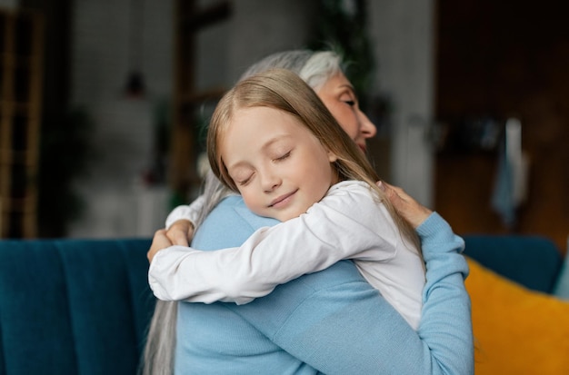 La bambina caucasica sorridente con gli occhi chiusi e gli abbracci della signora in pensione si godono insieme il momento tenero