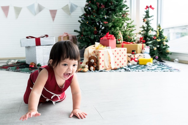 La bambina caucasica sta strisciando sul pavimento con la sfocatura degli alberi di Natale e molte scatole regalo