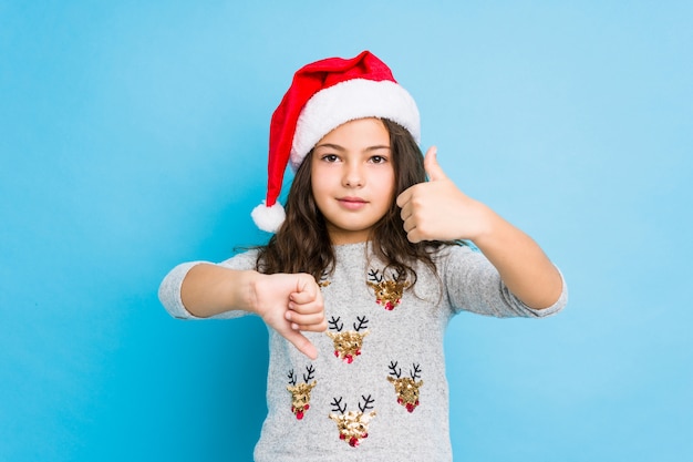 La bambina che celebra il giorno di Natale che mostra i pollici su e pollici giù, difficile sceglie il concetto