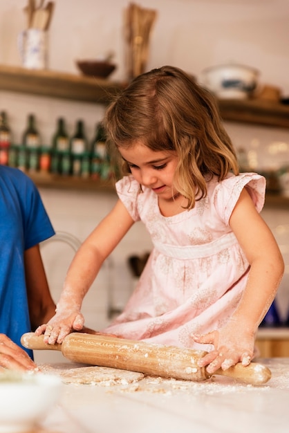 La bambina che impasta la pasta si prepara per cuocere i biscotti. Concetto di chef infantile.