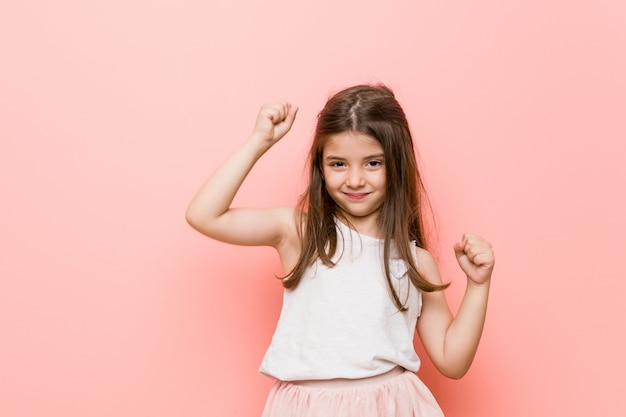 La bambina che indossa un look da principessa celebra un giorno speciale, salta e alza le braccia con energia.