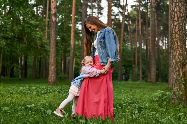 La bambina che ride felice abbraccia sua madre in piedi sull'erba nel parco