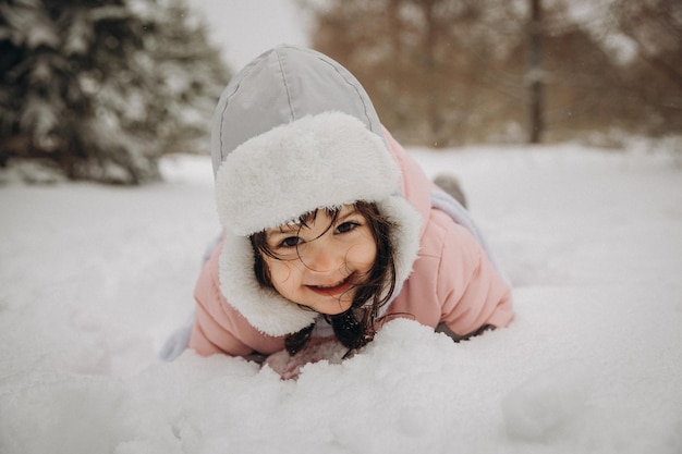 La bambina che ride in un caldo vestito invernale giace nella neve profonda.