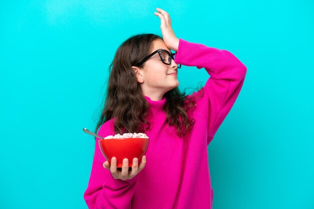 La bambina che tiene una ciotola di cereali isolata su sfondo blu ha realizzato qualcosa e intende la soluzione