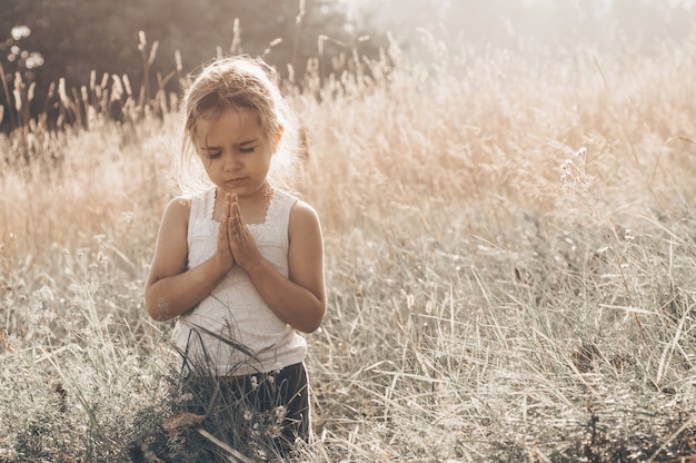 La bambina chiuse gli occhi, pregando all'aperto, le mani giunte nel concetto di preghiera per fede, spiritualità e religione. Pace, speranza, concetto di sogni.