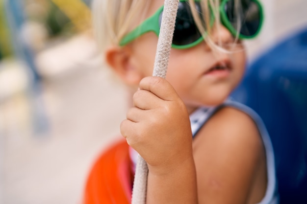 La bambina con gli occhiali da sole si aggrappa alla corda del ritratto dell'altalena