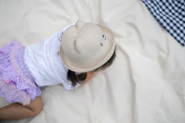 La bambina con il suo cappello sta strisciando sul panno color crema al campo all'aperto. Ripresa dalla vista dall'alto.