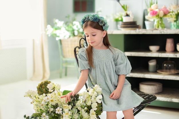 La bambina con in vestito si siede sulla sedia con i fiori in cucina