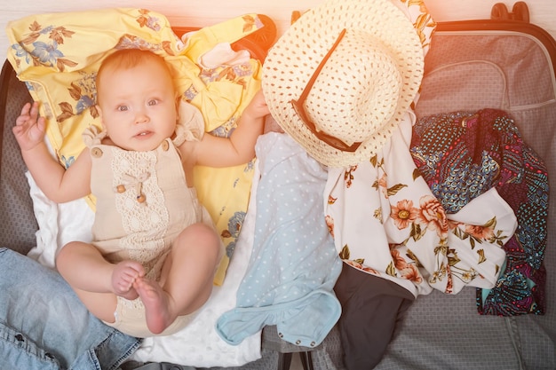 La bambina con l'espressione eccitata e divertita si trova in valigia con i vestiti e si prepara per l'estate v