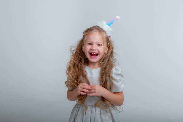 La bambina con un cappello da compleanno festeggia il suo compleanno su uno sfondo bianco