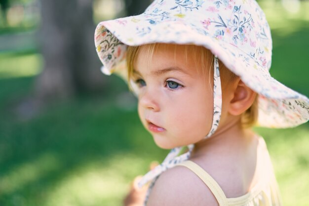 La bambina con un cappello panama si erge su un ritratto di prato verde