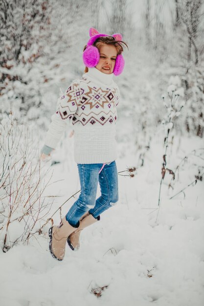 La bambina con un maglione e le cuffie invernali salta e si diverte in una giornata invernale.