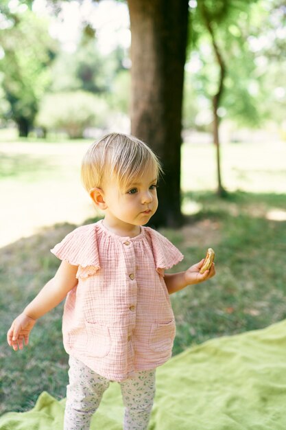 La bambina con un pancake in mano sta su una coperta su un prato verde