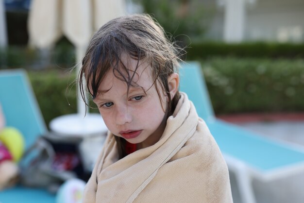 La bambina congelata si siede sulla spiaggia in asciugamano