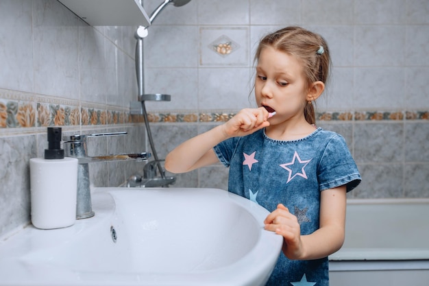 La bambina controlla l'igiene della sua bocca e si lava i denti in bagno vicino al lavandino bianco