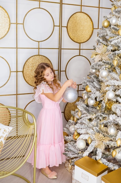 La bambina decora l'albero di natale, concetto del nuovo anno. Kid vicino all'albero di natale, ragazza in abito rosa.