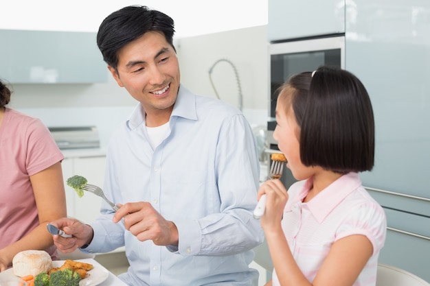 La bambina di sorveglianza del padre mangia l&#39;alimento con una forcella in cucina