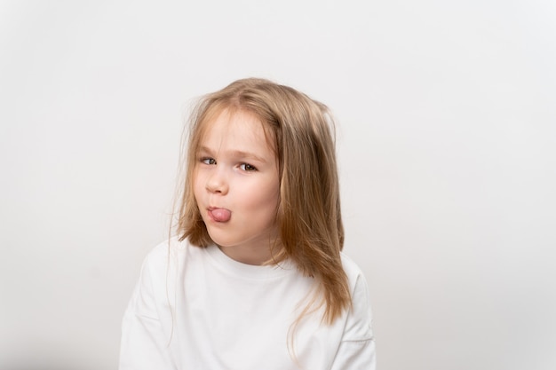 La bambina divertente mostra la lingua su un fondo bianco. infanzia felice. vitamine e medicine per il bambino.