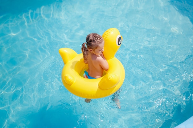 La bambina divertente nuota in uno stagno in un conservatore di vita giallo