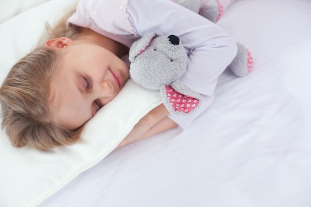 La bambina dorme nel letto con un orsacchiotto giocattolo