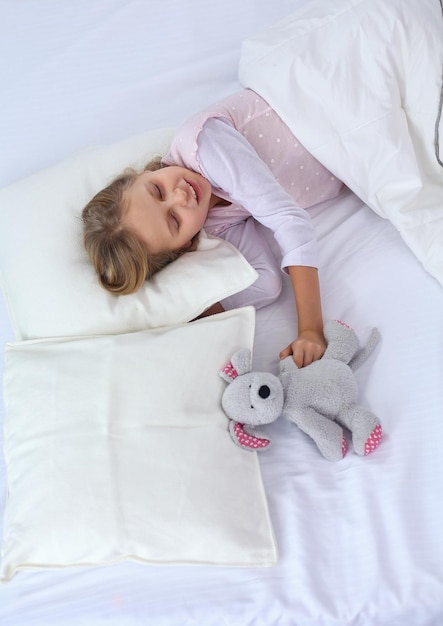 La bambina dorme nel letto con un orsacchiotto giocattolo