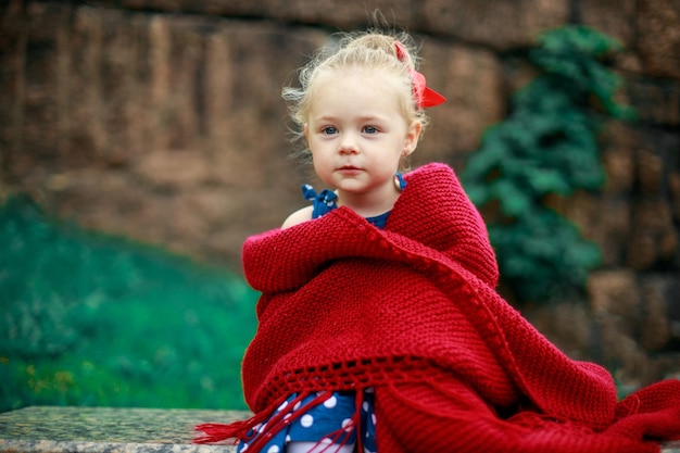 La bambina è avvolta in una coperta di lana rossa.