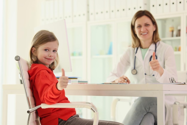 La bambina e il medico mostrano i pollici in su all'appuntamento nel pediatra dell'ufficio della clinica