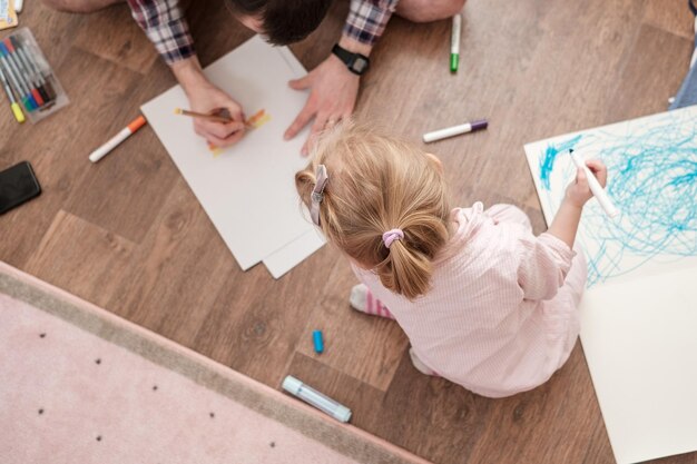 La bambina e il padre disegnano con pennarelli colorati seduti per terra nella stanza