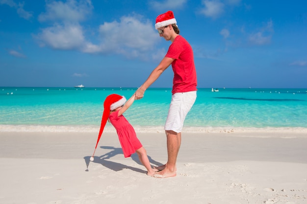 La bambina e il papà felice in Santa Hat si divertono alla spiaggia tropicale