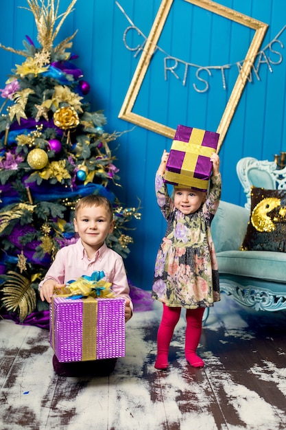 La bambina e il ragazzo svegli stanno sorridendo e stanno tenendo i regali sotto l'albero di Natale