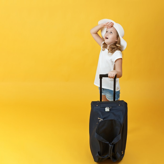 La bambina è pronta a viaggiare, si alza con una valigia e alza lo sguardo