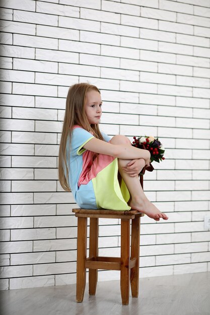 la bambina è seduta su una sedia e posa sulla telecamera