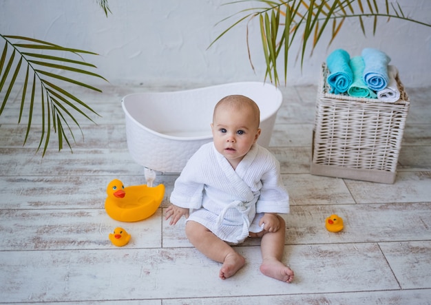 La bambina è seduta sul pavimento in un accappatoio bianco con accanto un bagnetto in ceramica. Igiene dei bambini